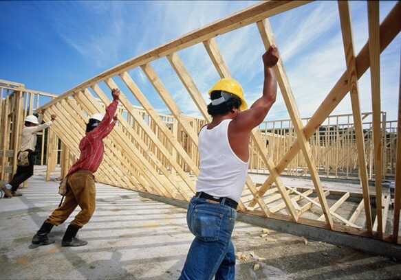 975254-001 Construction workers lifting up wooden frame of house, rear view